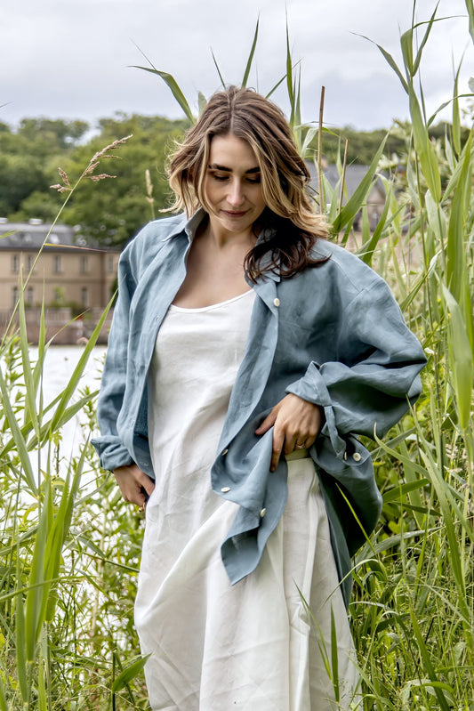 Eine Frau am See mit einer blauen Leinenbluse und einem hellgrauen Leinenkleid